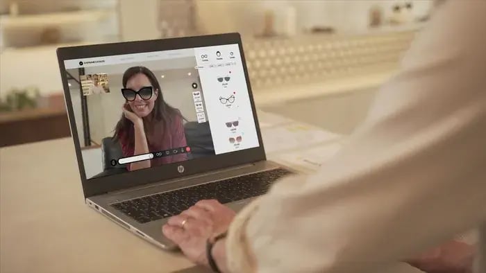 Person using a laptop to demonstrate virtual sunglasses try-on software.