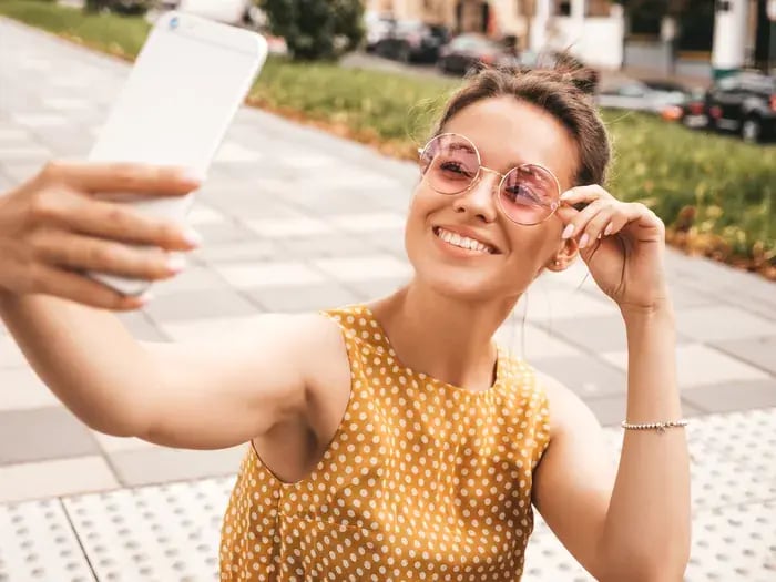 Smiling woman trying on sunglasses virtually through mobile app while sitting outside.