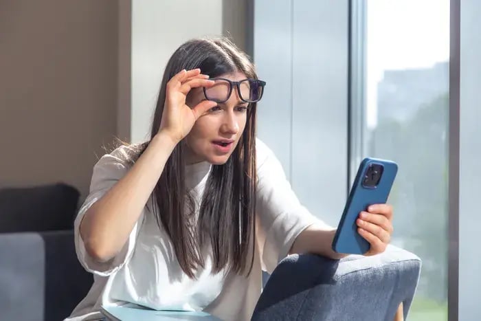 Woman reacting with surprise while using virtual try-on app to test eyeglass frames on smartphone.