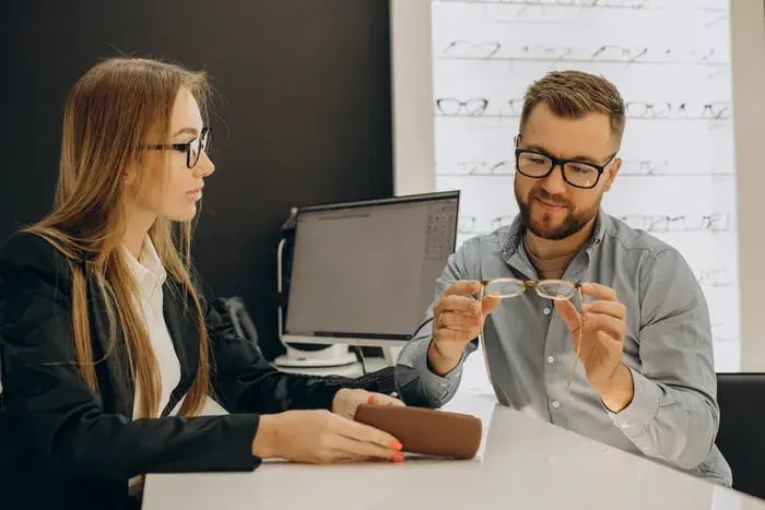 Optician assisting customer in selecting eyeglass frames with support from virtual try-on technology.