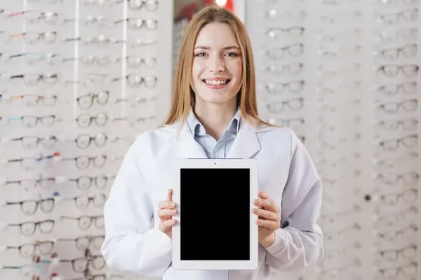 Optometrist showcasing a tablet-based kiosk for pupillary distance (PD) measurement in an eyewear store.