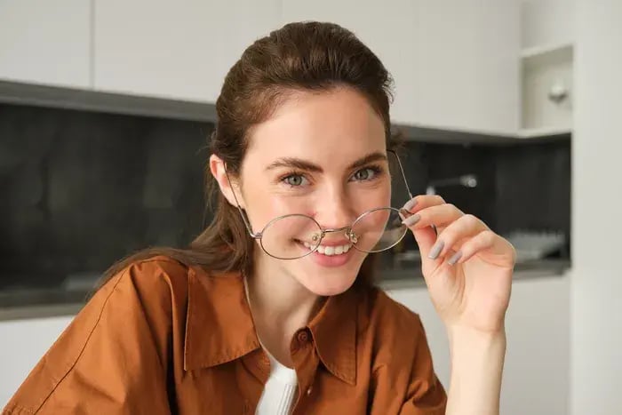 Woman smiling while wearing round eyeglasses, showcasing modern eyewear style.